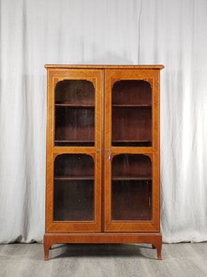 une vieille armoire en bois avec des portes vitrées et un rideau blanc derrière