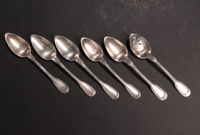 six cuillères en argent sont alignées sur une surface noire