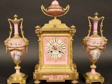 trois vases roses et dorés et une horloge posés sur une table