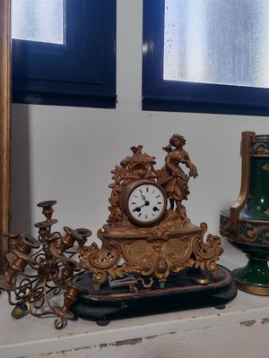 trois vases et une horloge posés sur une étagère devant une fenêtre