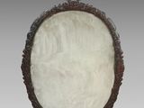 une plaque ovale en jade blanc, ornée de motifs sculptés, posée sur un socle