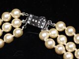 two strands of white pearls with a silver clasp on a black velvet surface