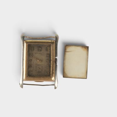 une petite montre carrée posée à côté d'une petite boîte