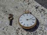 une montre de poche et une clé posées sur une surface en béton