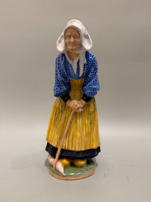 une vieille figurine représentant une femme avec un chapeau et une canne