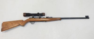 un fusil posé sur une surface blanche, équipé d'une lunette de visée