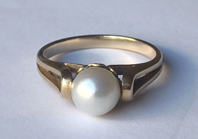 une bague ornée d'une perle au centre, sur un fond blanc