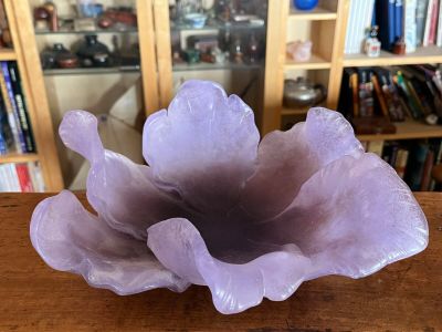 purple glass flower sitting on top of a wooden table in front of a bookshelf