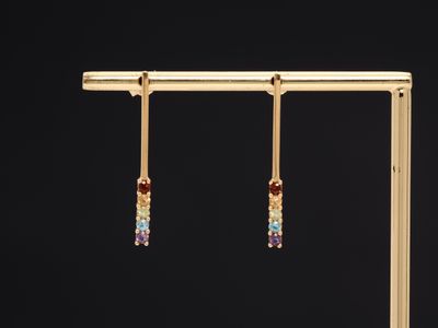 a pair of gold earrings with multi colored stones hanging from them
