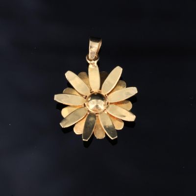 un gros plan d'un pendentif en forme de fleur dorée posé sur une surface noire