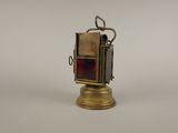 une vieille lanterne en laiton avec un verre rouge à l'intérieur, posée sur une surface blanche