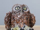 une figurine de chouette posée sur une table en bois, près d'un mur gris