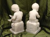 pair of white marble statues of a boy and a girl sitting on a box