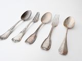 five silver spoons and two silver spoons on a white surface