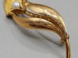 an image of a gold brooch with a pearl in the center