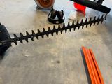 une taille-haie posée par terre à côté de quelques outils