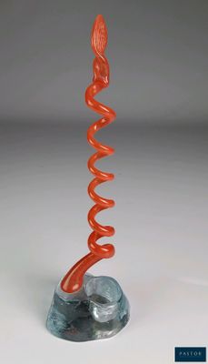 une sculpture en verre orange représentant un motif en spirale, posée sur un socle en marbre