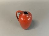 a red vase with a black handle on a white surface