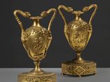 une paire de vases anciens en laiton, posés sur des socles, sur une table