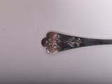 a silver spoon with a flower on it on a white surface