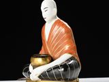 a statue of a person sitting on a table with a pot