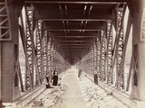 a black and white photo of two people walking on a bridge