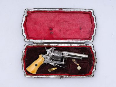 un revolver argenté dans un étui rouge posé sur une surface blanche
