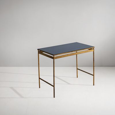 une table noire et dorée avec un plateau en verre, posée sur un socle blanc