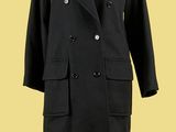 un manteau noir posé sur un mannequin, devant un fond jaune