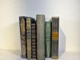 several old books are lined up on a shelf in front of a white wall