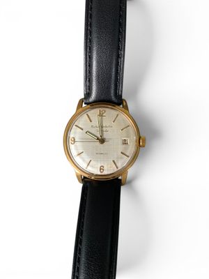 gros plan d'une montre sur une surface blanche avec un bracelet noir