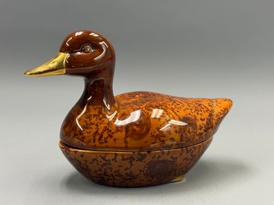 une petite boîte en forme de canard marron avec un bec doré