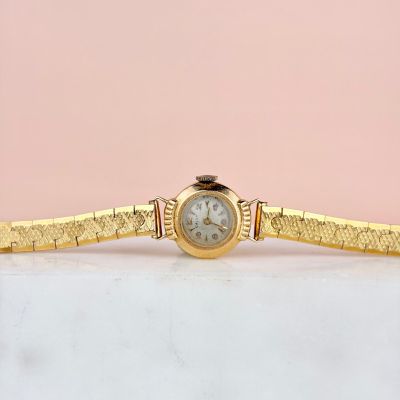 une montre-bracelet en or avec un cadran blanc posée sur une surface en marbre