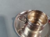 a silver cup and saucer sitting on a table