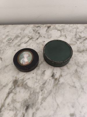une petite boîte noire avec un couvercle vert posée sur une table en marbre