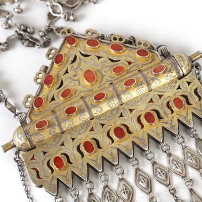 silver and gold necklace with red stones and chains on a white surface