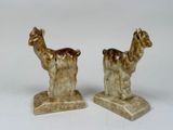 pair of ceramic figurines of llamas on stand on white background