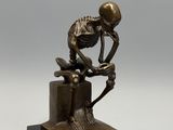 statue en bronze représentant un squelette assis sur une boîte avec un livre