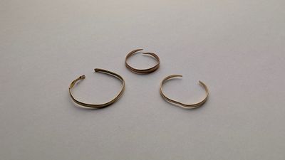 three pairs of gold hoop earrings sitting on top of a white surface