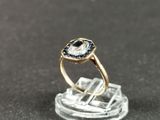 une photo d'une bague sertie d'un diamant et d'un saphir posée sur un morceau de verre transparent