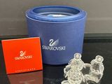 des figurines en cristal Swarovski dans une boîte bleue et une boîte rouge, posées sur une table noire