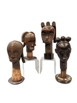 three wooden sculptures of heads on stands on a white surface