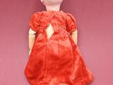 doll with red dress and brown shoes laying on a pink surface