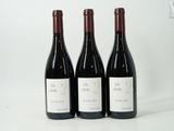 trois bouteilles de vin rouge sont alignées sur une surface blanche