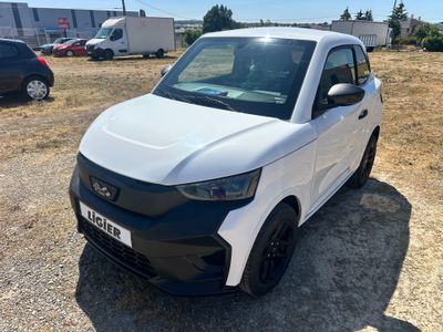 La petite voiture blanche est garée sur un parking, avec d'autres voitures en arrière-plan.