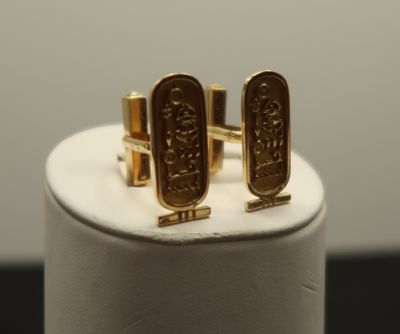 two gold cufflinks with egyptian symbols on them on a white stand