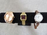 three watches on a black display stand with a white background