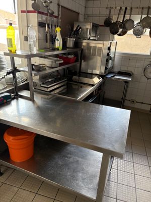 une table en acier inoxydable sur laquelle sont posés des casseroles et des poêles, dans une cuisine