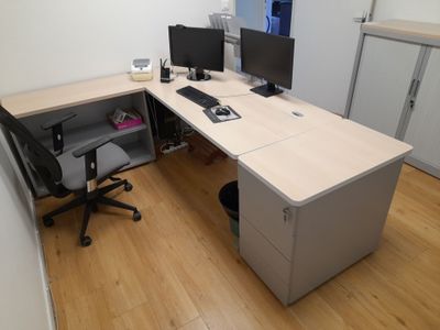 a desk with two computers and a chair in the corner