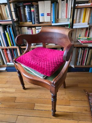 une chaise en bois avec un coussin rose devant une bibliothèque